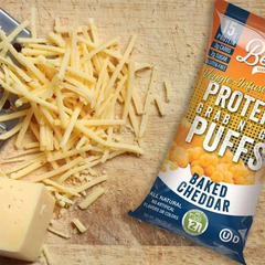 Keto Store NZ | Better Than Good Foods | Protein Grab and Go Puffs Baked Cheddar | Veggie-infused | Baked Cheddar protein puffs package on a wooden surface with shredded cheese and a block of cheese.